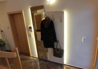 Gästegarderobe weiß lackiert, in Kombination mit Zebrano Wandpaneel mit Spiegel und indirekter Wandbeleuchtung.