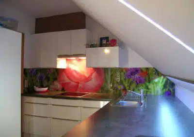 Einbauküche unter Dachschräge. Glaswandschoner mit Blumenmotiv.