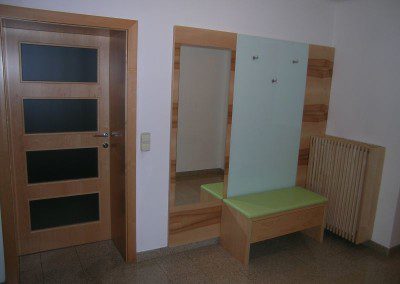 Garderobenwand mit Kernahorn furniert kombiniert mit lacobel Glas, Sitzgelegenheit mit Lade und Heizkörperverbau.